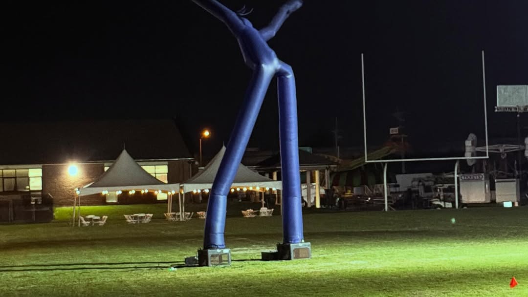Illuminated blue Fly Guy and bistro-lit event tents at a night fair